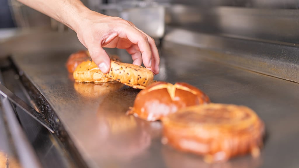 Gros plan sur des pains à burger en train de griller sur la plaque chauffante en acier inoxydable d'une cuisine professionnelle.