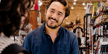 Close-up of a friendly man with a beard smiling at someone in a small retail shop.