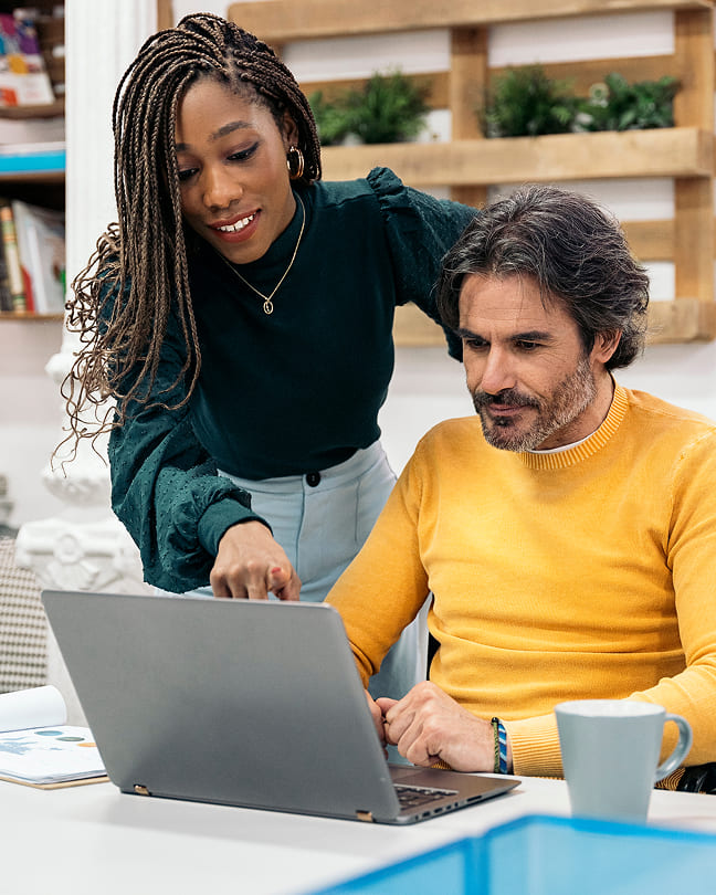 Woman leaning over to point at a screen while helping a seated colleague.