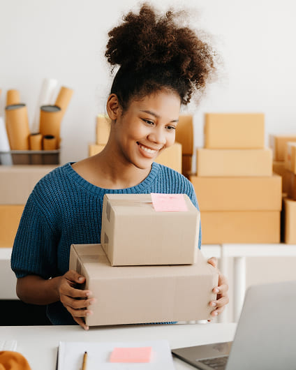 Young woman preparing cardboard packages for shipping near her laptop.