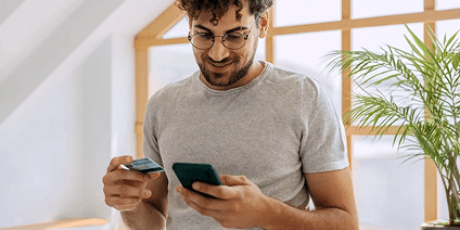 Man in his home looking at credit card and phone while smiling