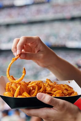 Person holding a paper tray of curly fries at a stadium event.