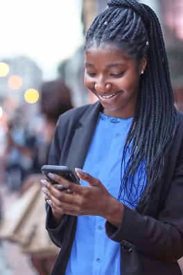 Young woman with braids typing on her smartphone with a smile.