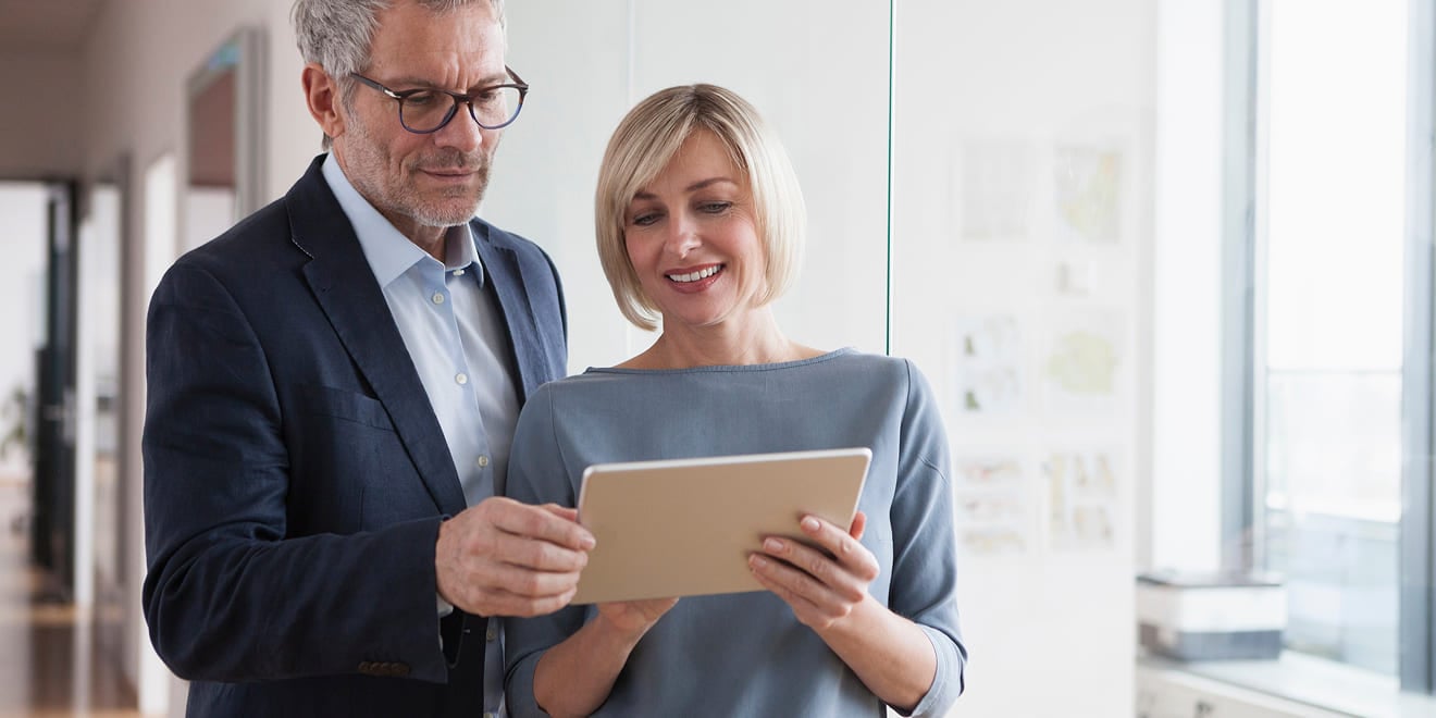 Man in a suit and blonde woman reviewing information on a digital tablet.