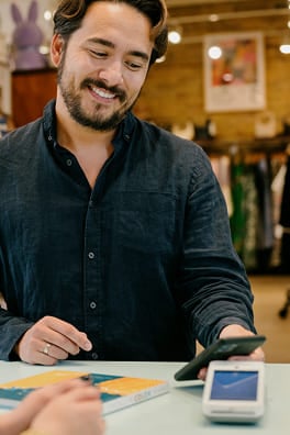 Customer tapping phone to pay at a card terminal in a boutique store.