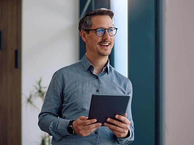 A professional looking out a window while holding a tablet device
