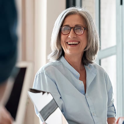 Professional woman in a light blue shirt smiling in a modern office.