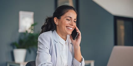 Woman in a blazer smiling while having a smartphone call at work.