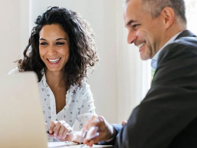 Woman and man in a business meeting smiling at a laptop screen together.