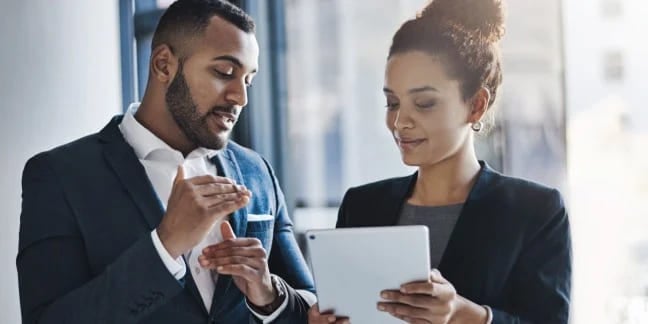 Man and woman in professional suits collaborating over a tablet device.