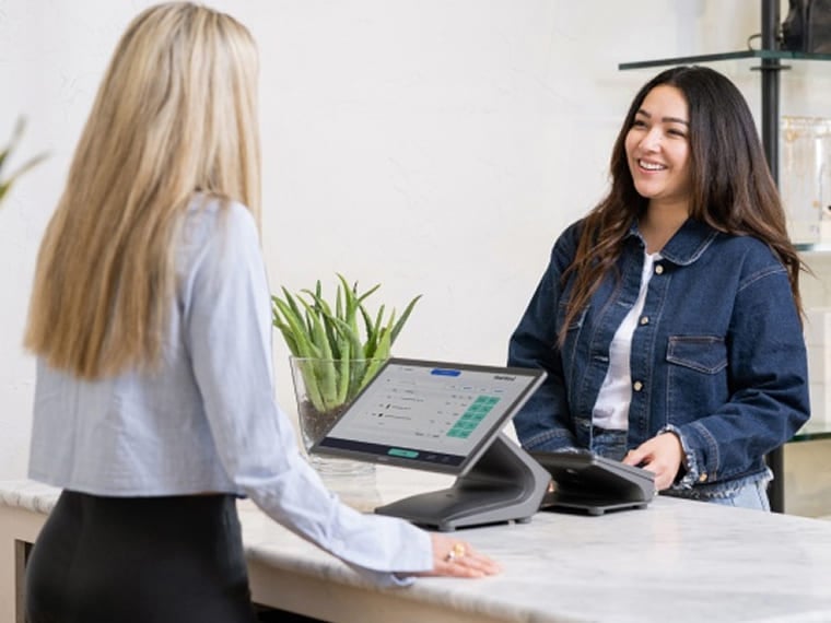 Customer standing at a checkout counter while a cashier uses a touchscreen POS system.