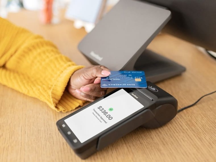 Person tapping a payment card on a terminal showing an approved transaction.
