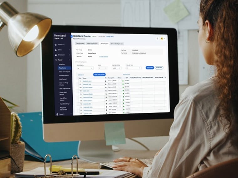 Person sitting at a desk reviewing payroll data on a desktop screen.