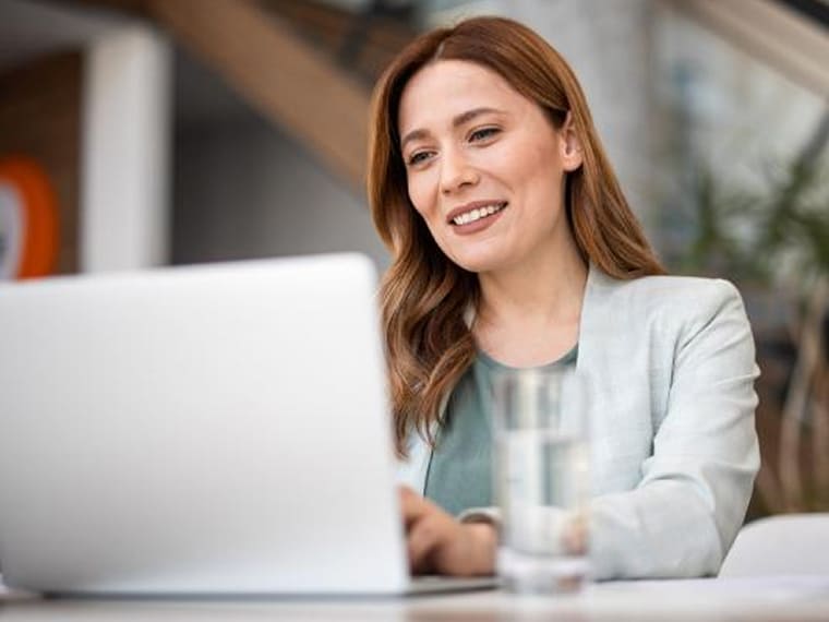Woman in a blazer typing on her laptop computer with a smile.