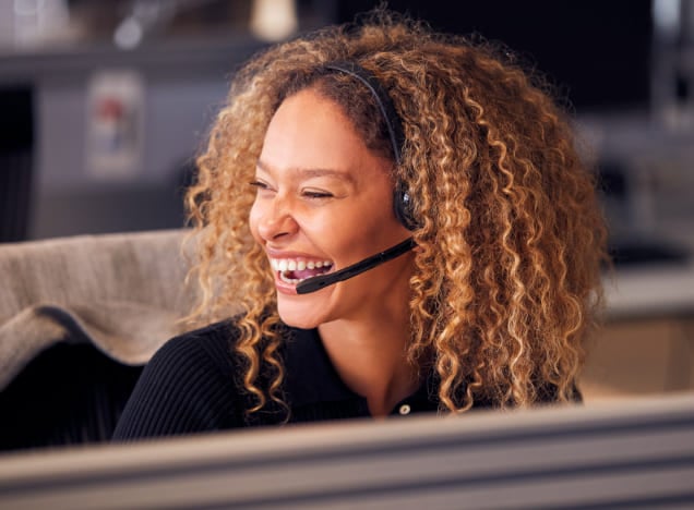 Woman with curly blonde hair wearing a phone headset and laughing at her desk