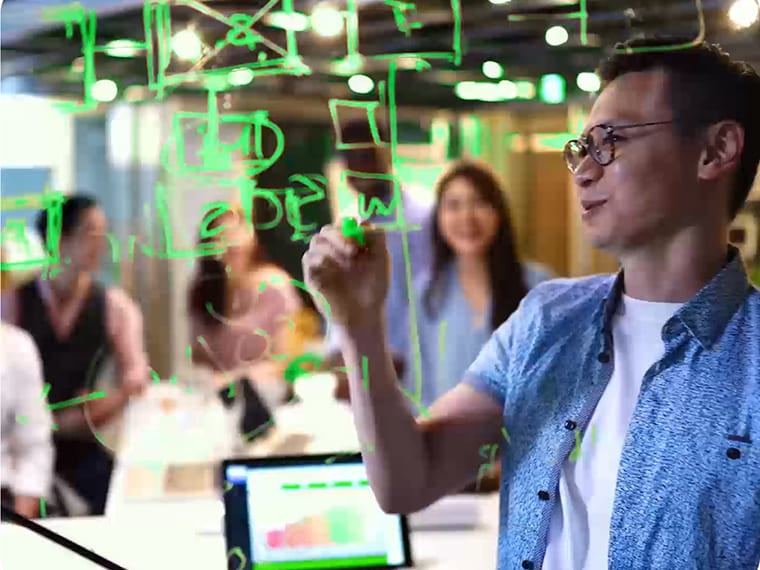 Man writing flowcharts on a clear glass board during a team meeting
