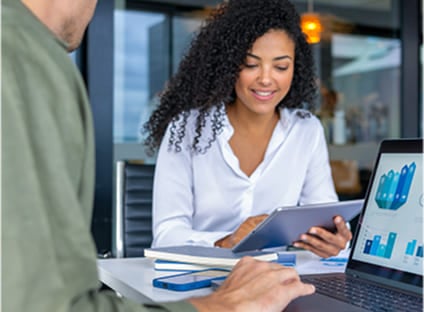 Two professionals reviewing business data and charts on a laptop and tablet