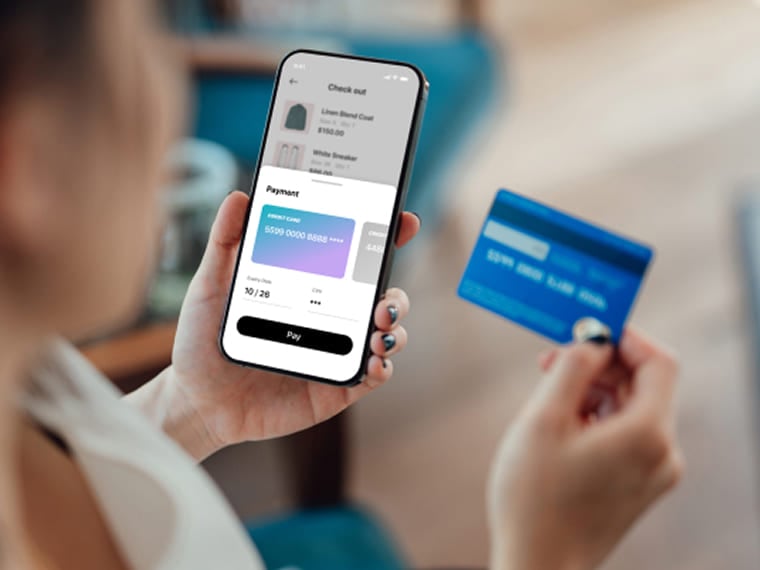Person holding a smartphone on a checkout screen and a blue credit card.