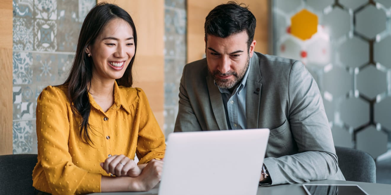 Smiling woman and businessman reviewing work together on a laptop.