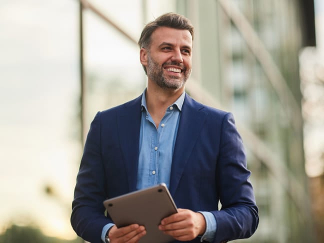 Professional man in a suit holding a tablet outside an office building.