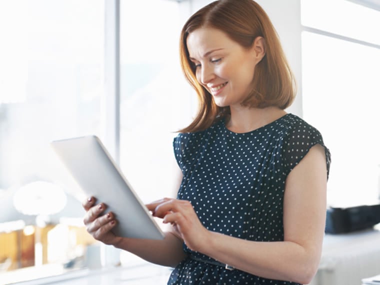 Woman smiling while working on a digital tablet in a bright office.