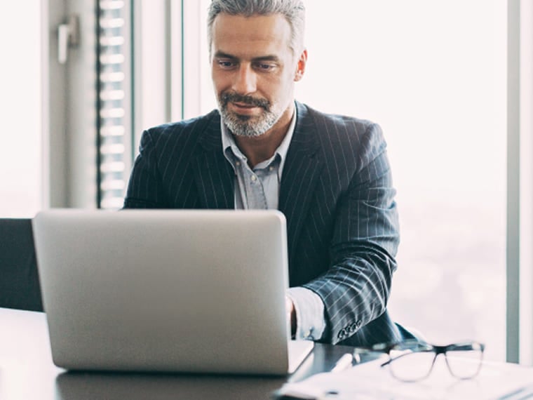 Professional man in a suit working on a laptop with glasses on desk.