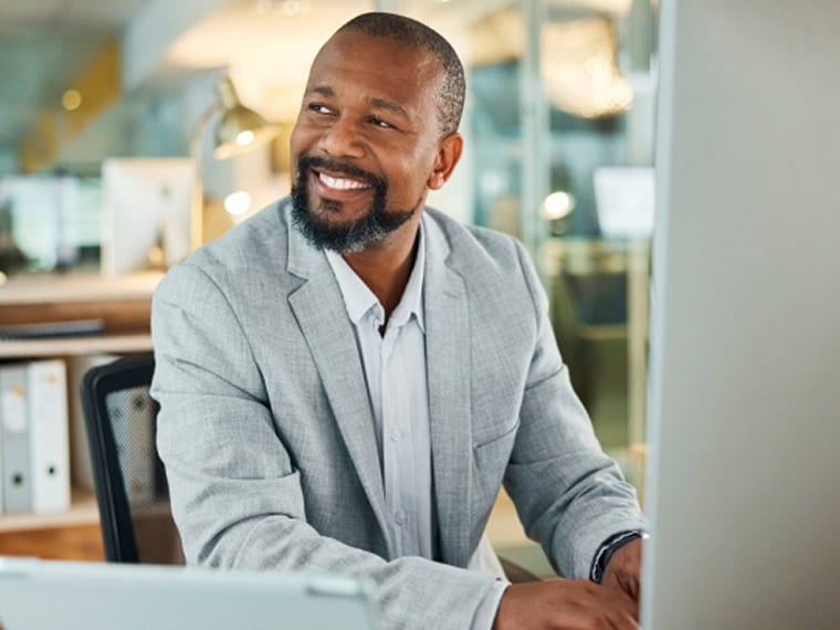 Professional man smiling while working on a computer at his desk.