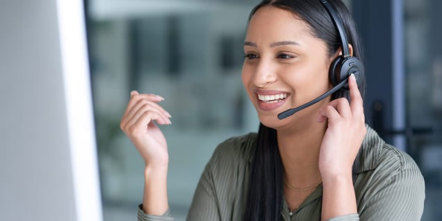 A woman wearing a headset gesturing while speaking to a client.