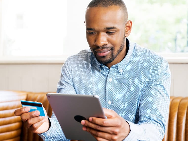 Man holding a credit card while using a digital tablet.