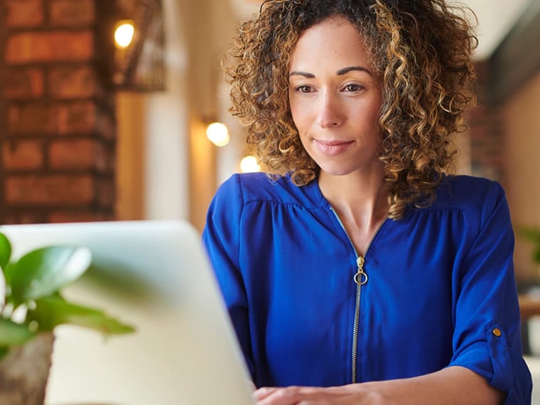 Woman with curly hair working on her laptop in a brightly lit space