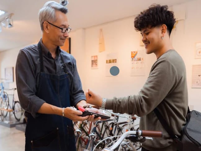 Young man using smartwatch contactless payment at a bike shop counter.
