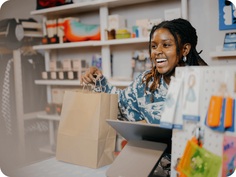 Worker hands customer their purchase in a bag after checking out at the countertop point of sale.