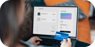 A person holding a blue credit card while making an online purchase on a laptop.