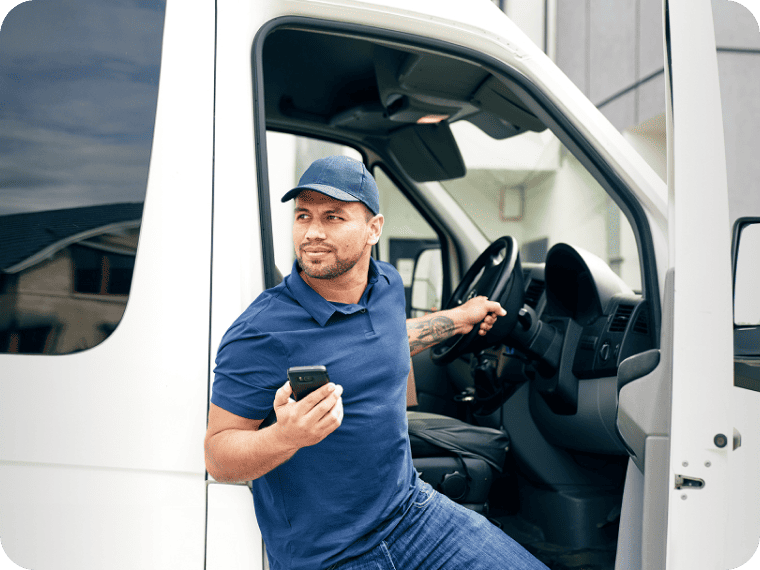 Service worker holding a mobile phone in the driver's seat of an open white delivery van.