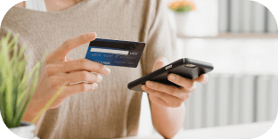 Hands holding a credit card and mobile phone to complete an online transaction.