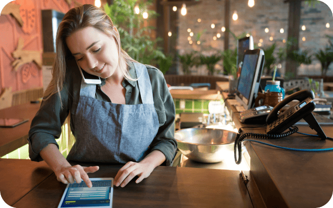 Restaurant employee speaking on the phone and entering data on a tablet.