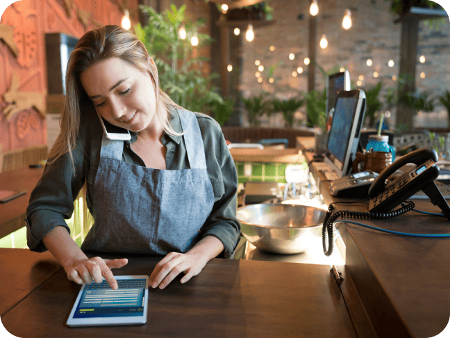 Restaurant employee speaking on the phone and entering data on a tablet.