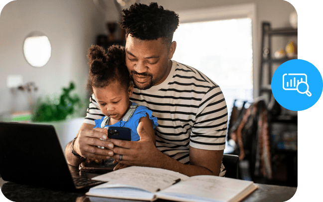A parent holds a baby over a desktop, while studying.