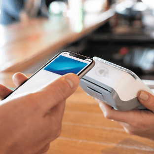 A customer swipes a phone over a card machine to make a payment.