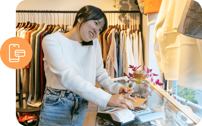 A clothing retailer takes a payment while talking on a mobile phone.