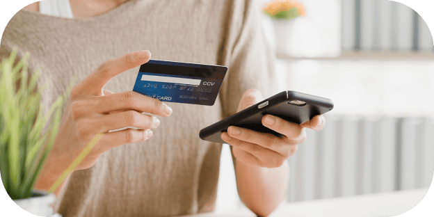 Persona que sostiene una tarjeta de crédito y un teléfono inteligente mientras realiza un pago en línea.