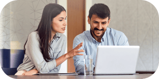 A woman explaining something to a smiling male colleague looking at a laptop screen.