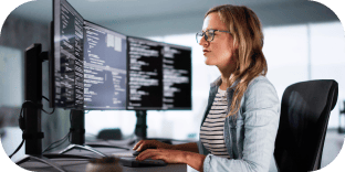 A woman in an office looks at several large computer monitors.