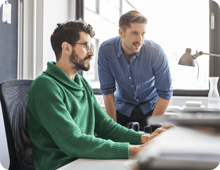 Two colleagues collaborating at a computer desk in a bright, modern office space.