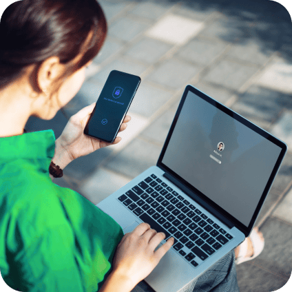 Woman verifying security on her smartphone while logging into a laptop outdoors.