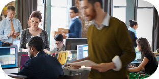 A busy workplace shows several people sitting at computers or moving around the office carrying stacks of paper or using smartphones.
