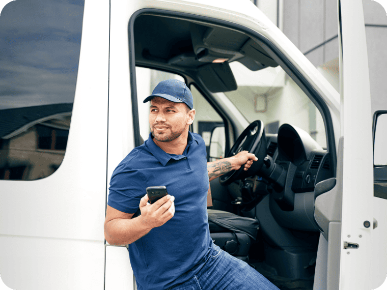 A person making deliveries holds a smartphone and exits the delivery vehicle. 