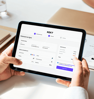 Mains tenant une tablette affichant l'écran de paiement en ligne de NEXT.