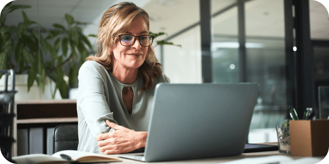 Professional woman wearing glasses working on a laptop at her desk in an office.