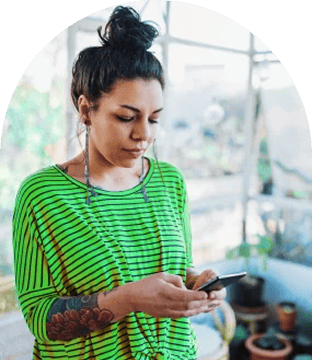 Woman in a green striped shirt with hair in a bun typing on her smartphone.